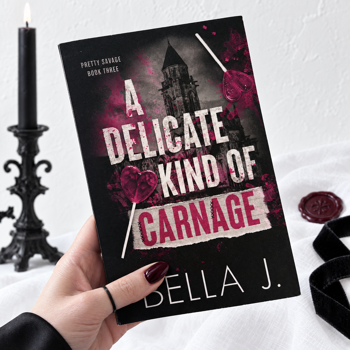 Hand holding a signed paperback of A Delicate Kind of Carnage by Bella J., Pretty Savage book 3