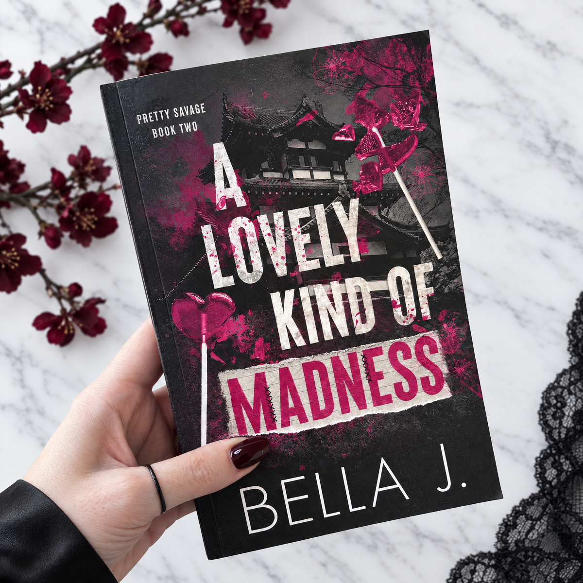 Hand holding a signed paperback of A Lovely Kind of Madness by Bella J., Pretty Savage book 2