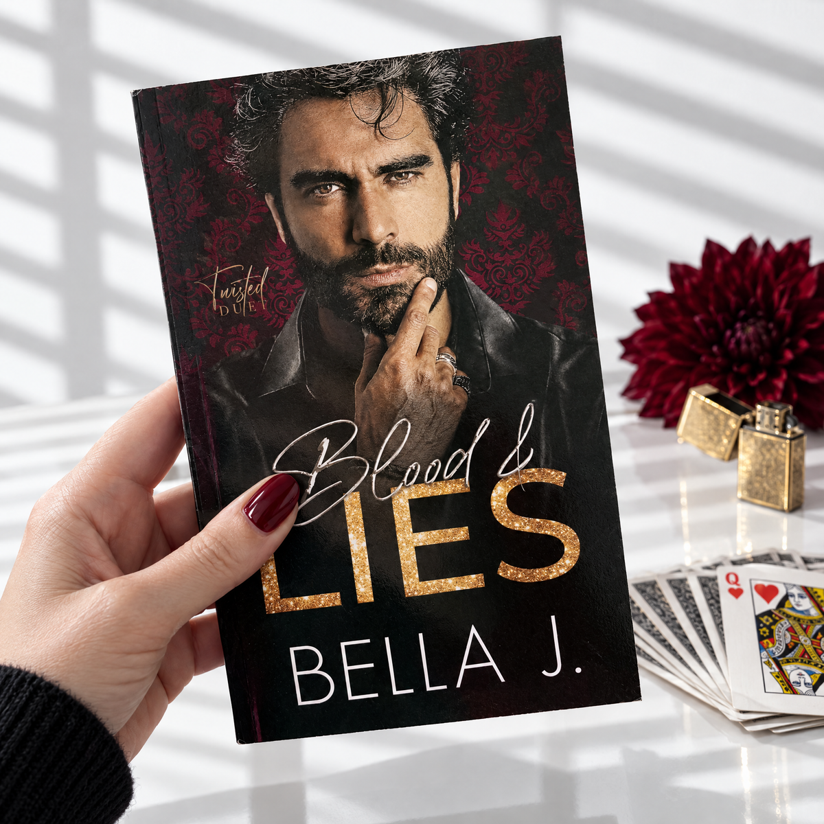 Hand holding a signed paperback of Blood and Lies by Bella J., model cover, Twisted Duet book 1